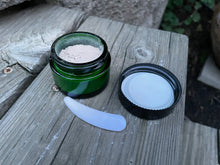 an open jar of facial clay with white lid on top of picnic table