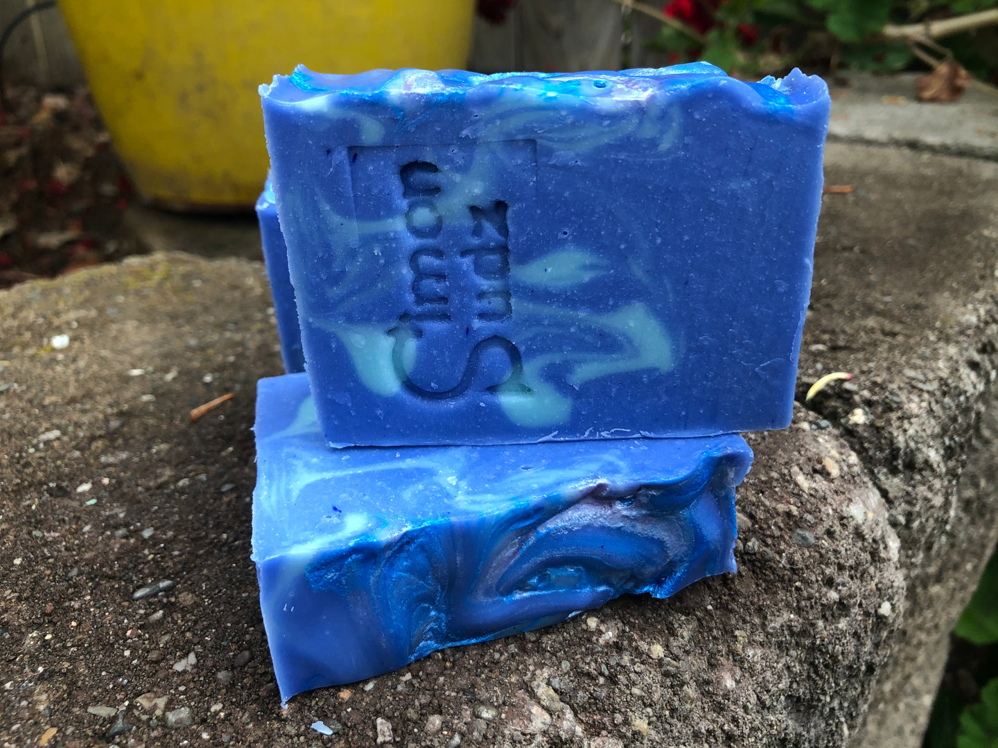 three blue soap bars in a backyard with words simon sudz stamped onto the front